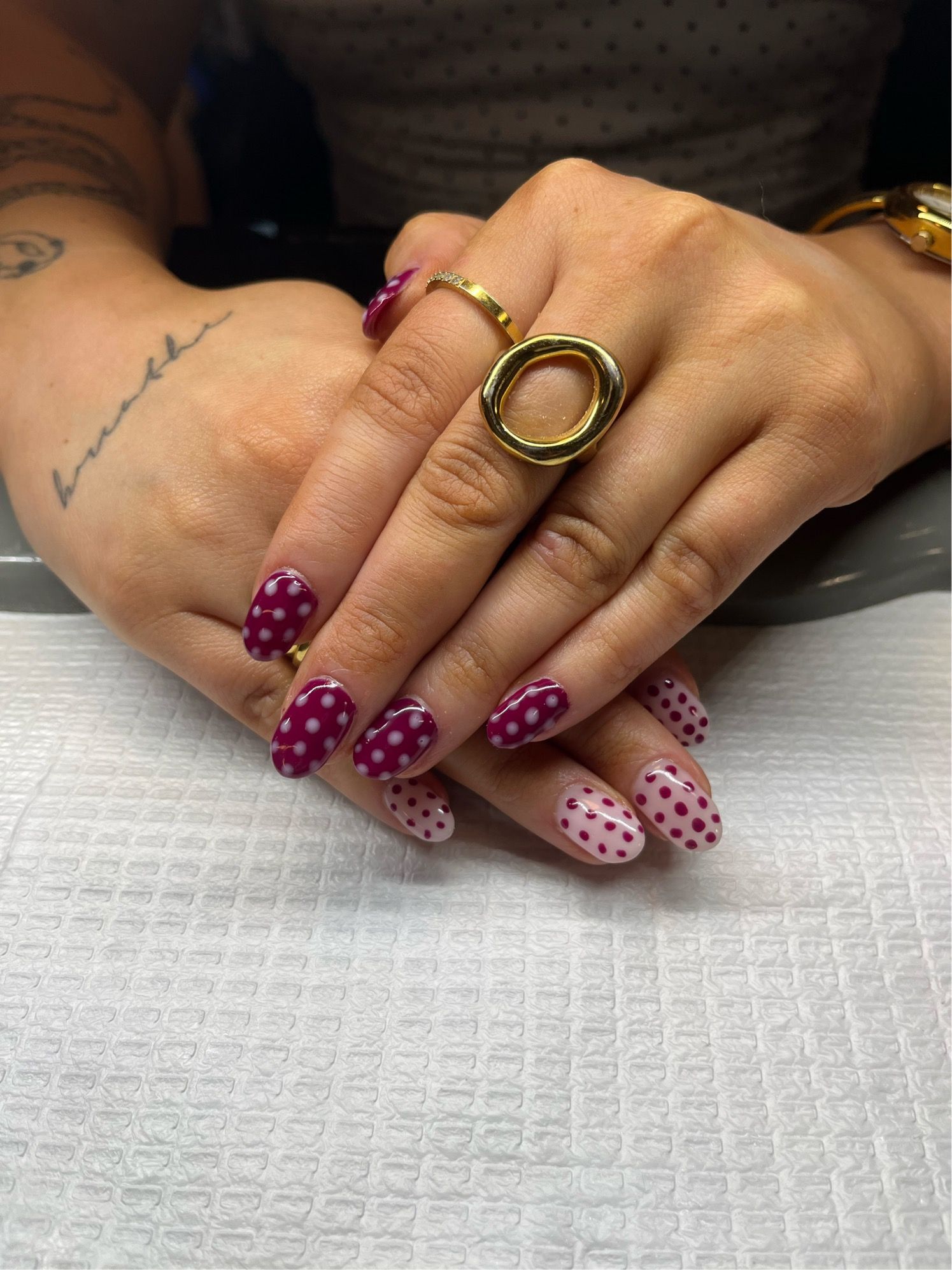Hands with purple and pink polka dot manicured nails and gold rings resting on a table