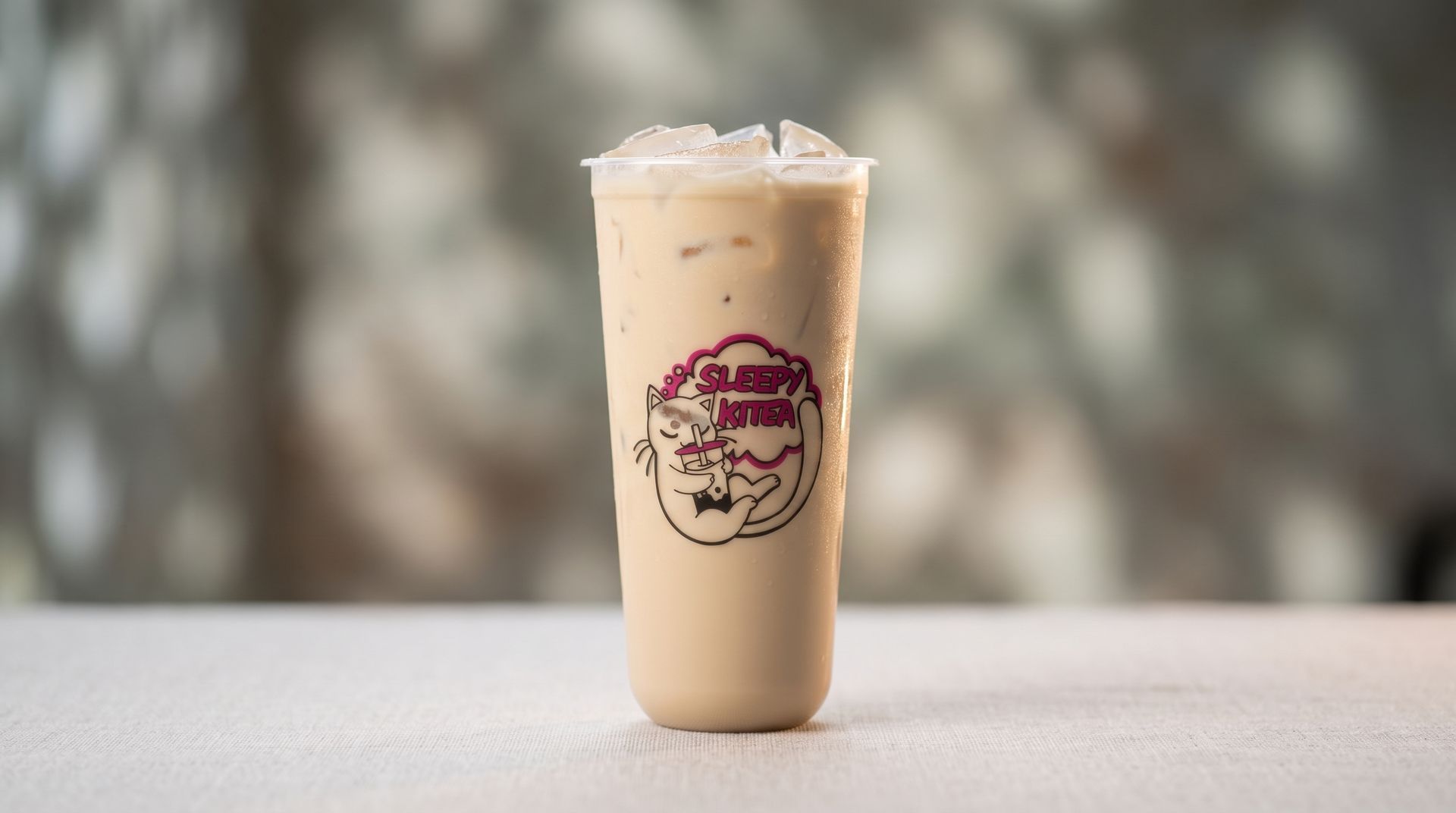 Iced beige drink in a clear plastic cup with a pink logo on a table against a blurred background