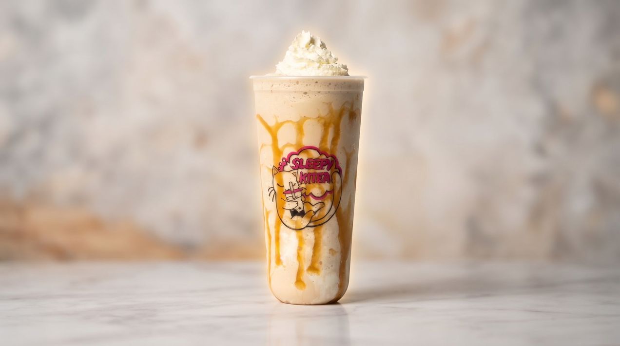 Tall iced dessert drink with whipped cream and caramel drizzle in a clear glass on a light table