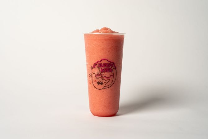 A yellow smoothie in a clear cup with a cartoon logo, standing on a neutral backdrop.