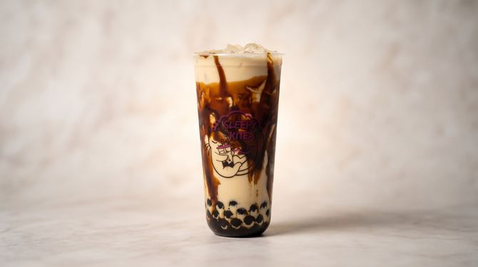 Iced bubble tea in a clear glass, with dark syrup swirling through milk and tapioca pearls at the bottom.