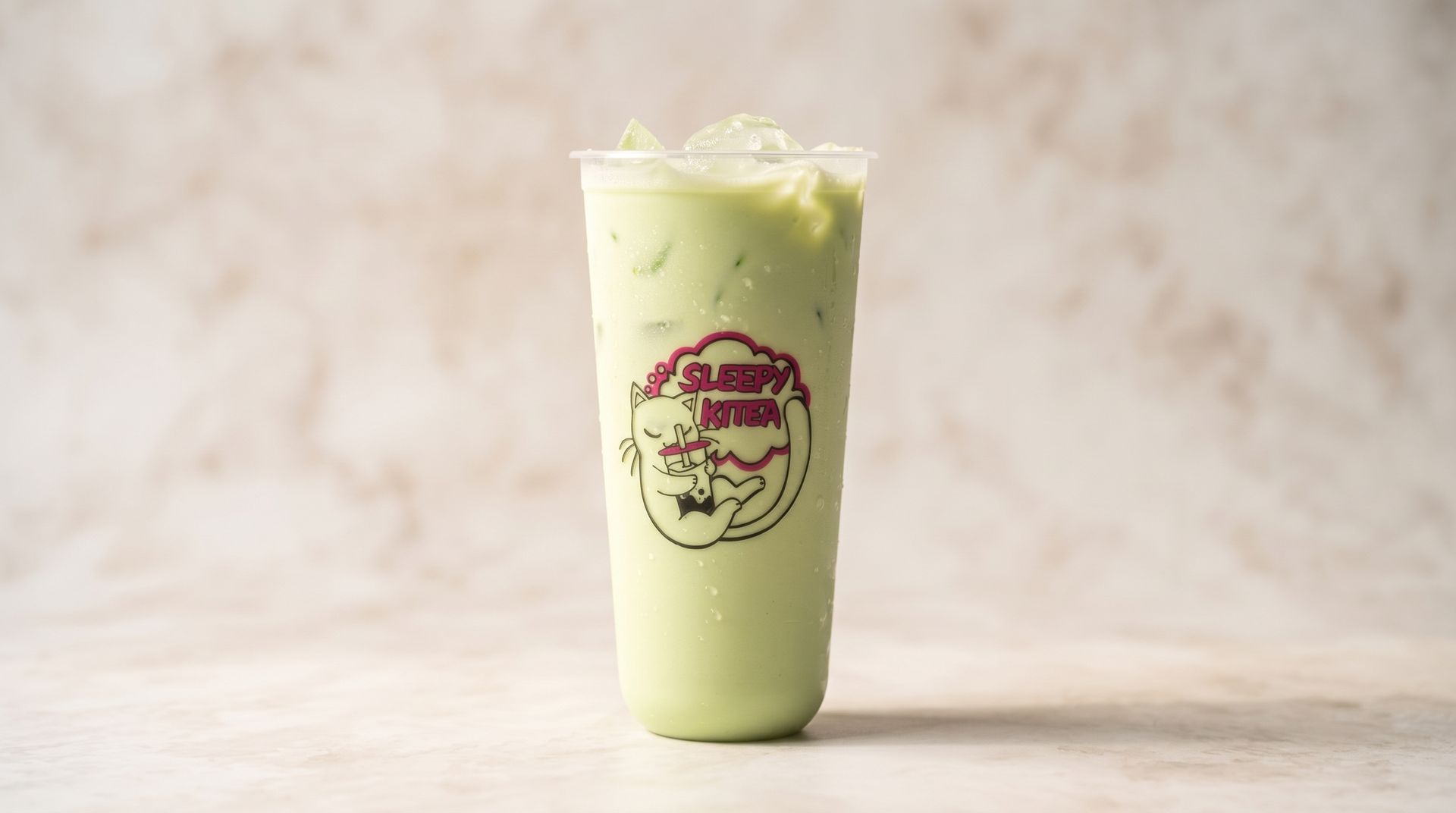 Tall pale green iced drink in a clear cup with a logo, centered on a light marble background