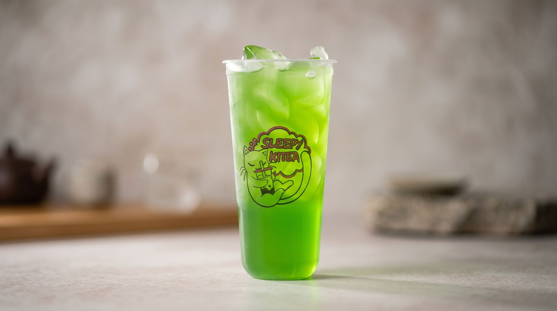 Bright green iced drink in a clear plastic cup on a tabletop, with a blurred café background