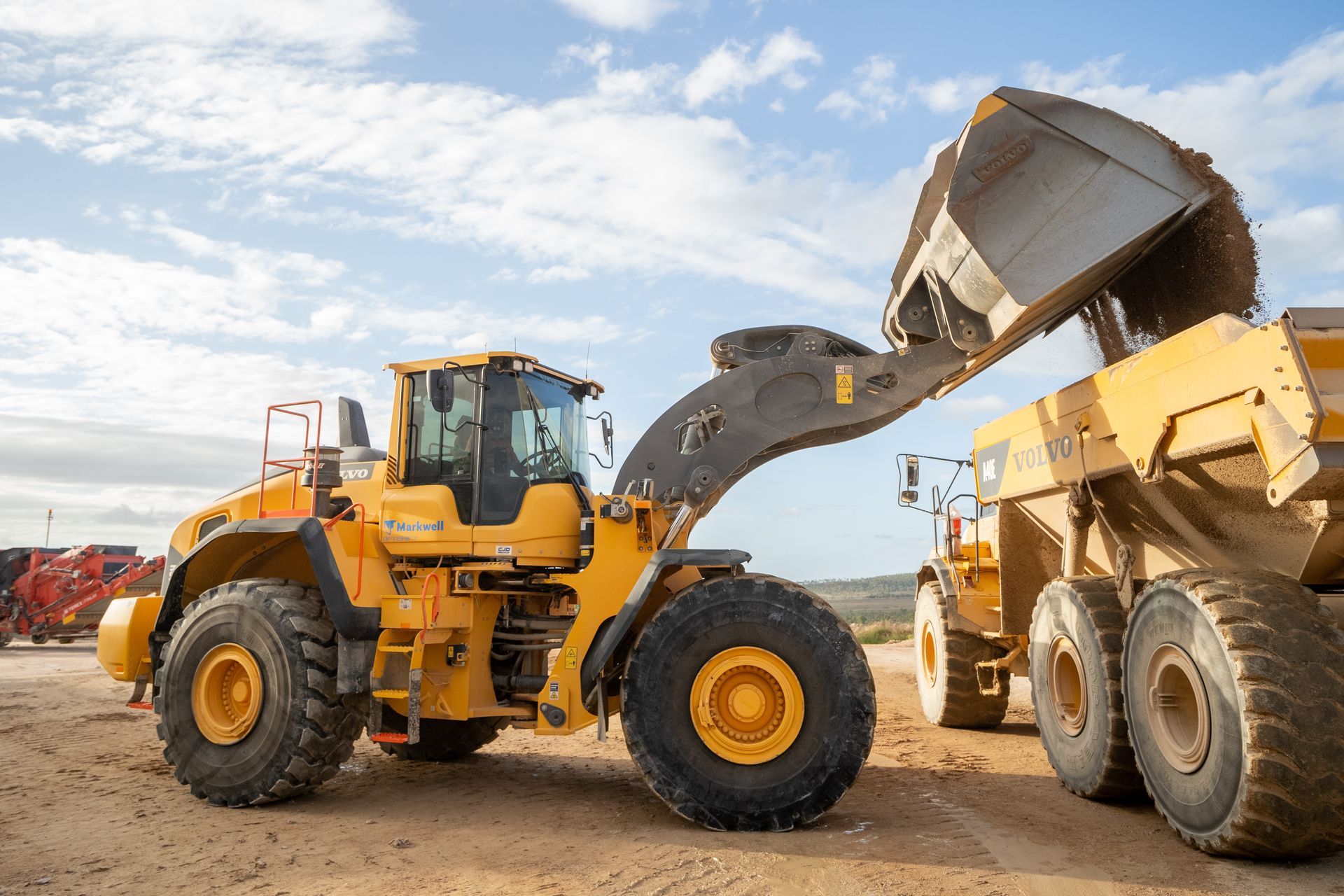 A bulldozer is loading dirt into a dump truck.