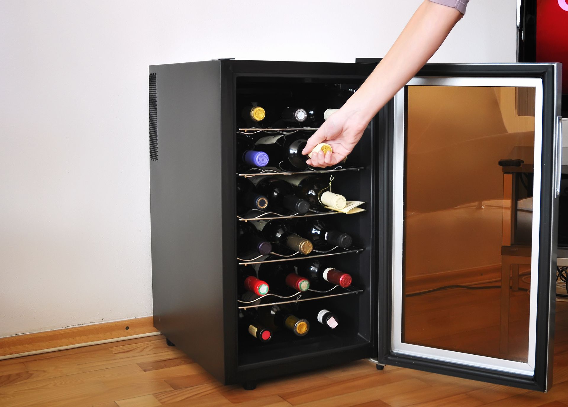 A person is opening a wine cooler filled with wine bottles.