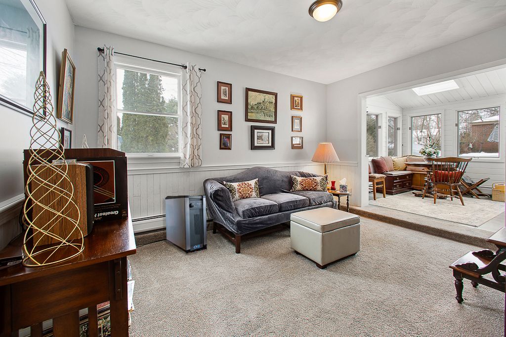 Bright living room with blue sofa, patterned chair, lamp, framed art, and dining area beyond the doorway