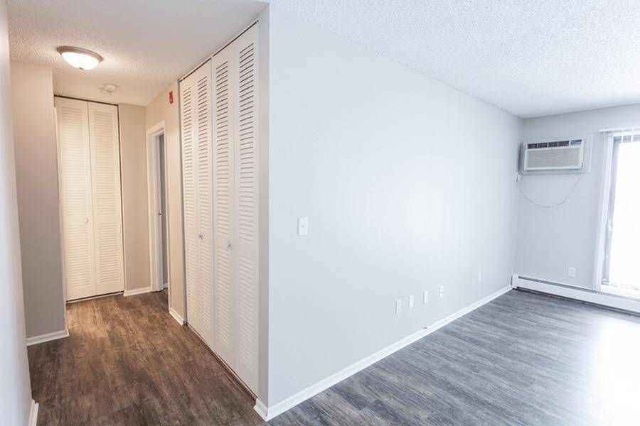 Hallway and living area of an unfurnished apartment with closets and a window AC unit.