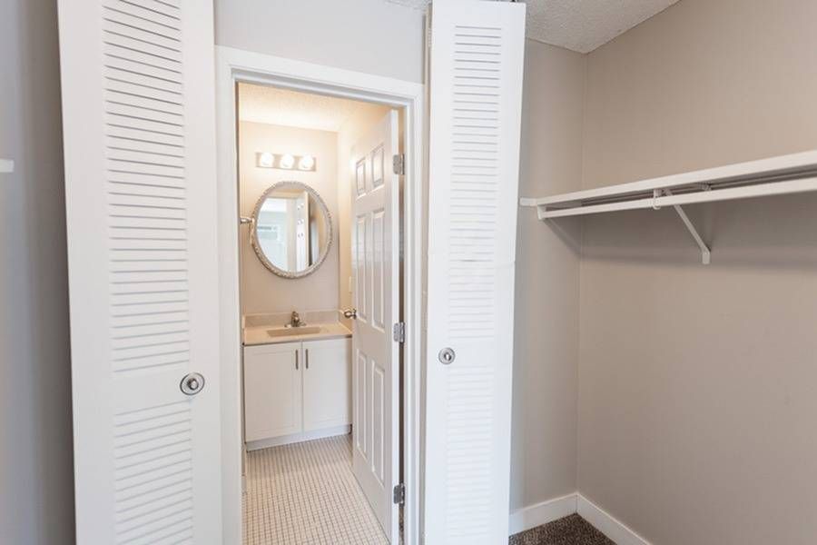 Small apartment bathroom with white vanity, round mirror, and a closet with a hanging rod.