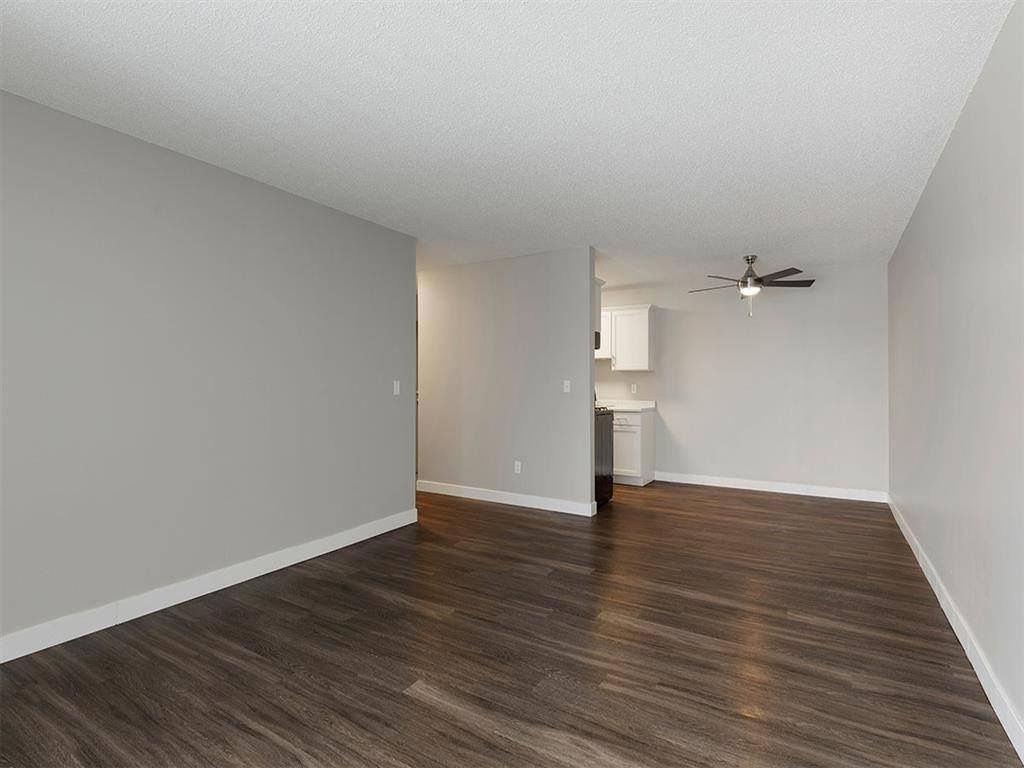 Empty apartment living area with gray walls, dark wood-look floors, and an open kitchen.