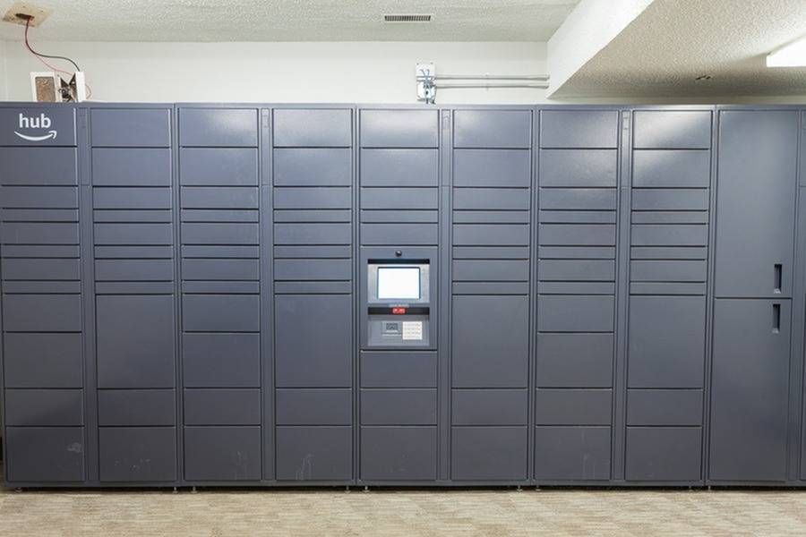 Row of dark blue package lockers in a hallway with a central touchscreen panel.