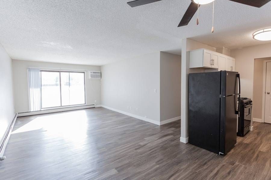 Open living area with large window, light gray walls, and adjacent kitchen with black appliances.