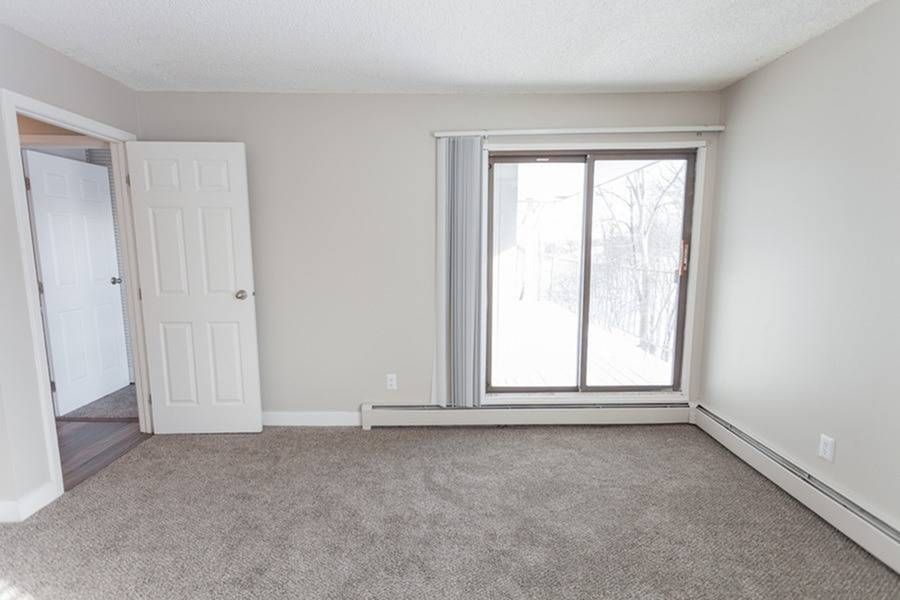 Empty living room with beige walls, carpet, and a sliding glass door to the outdoors.