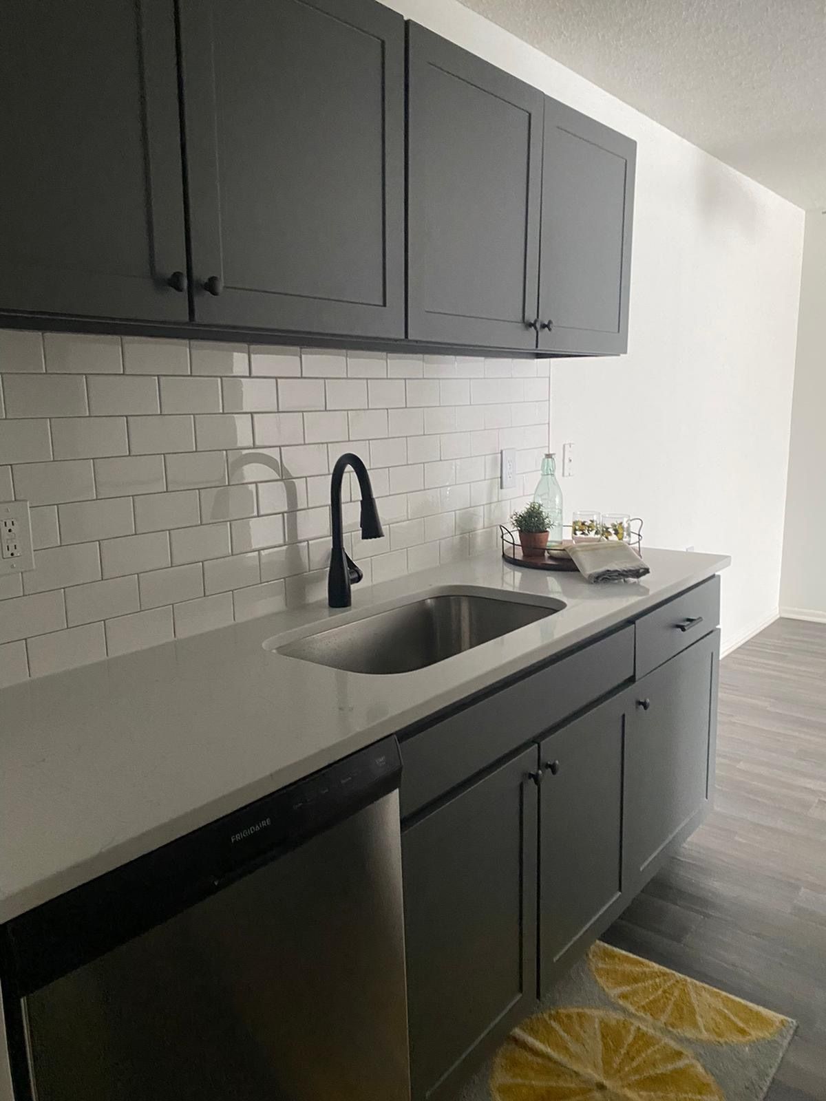 Modern apartment kitchen with gray cabinets, white subway tile backsplash, and stainless steel sink.