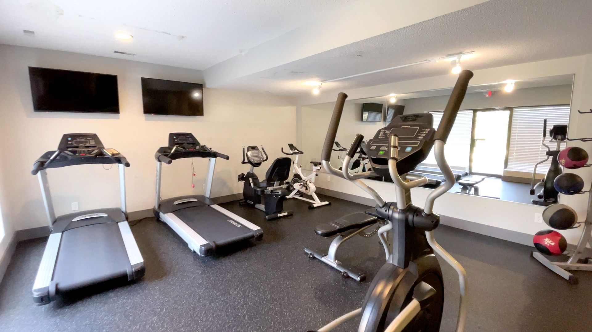 Bright gym with treadmills, stationary bikes, and exercise equipment on a carpeted floor.