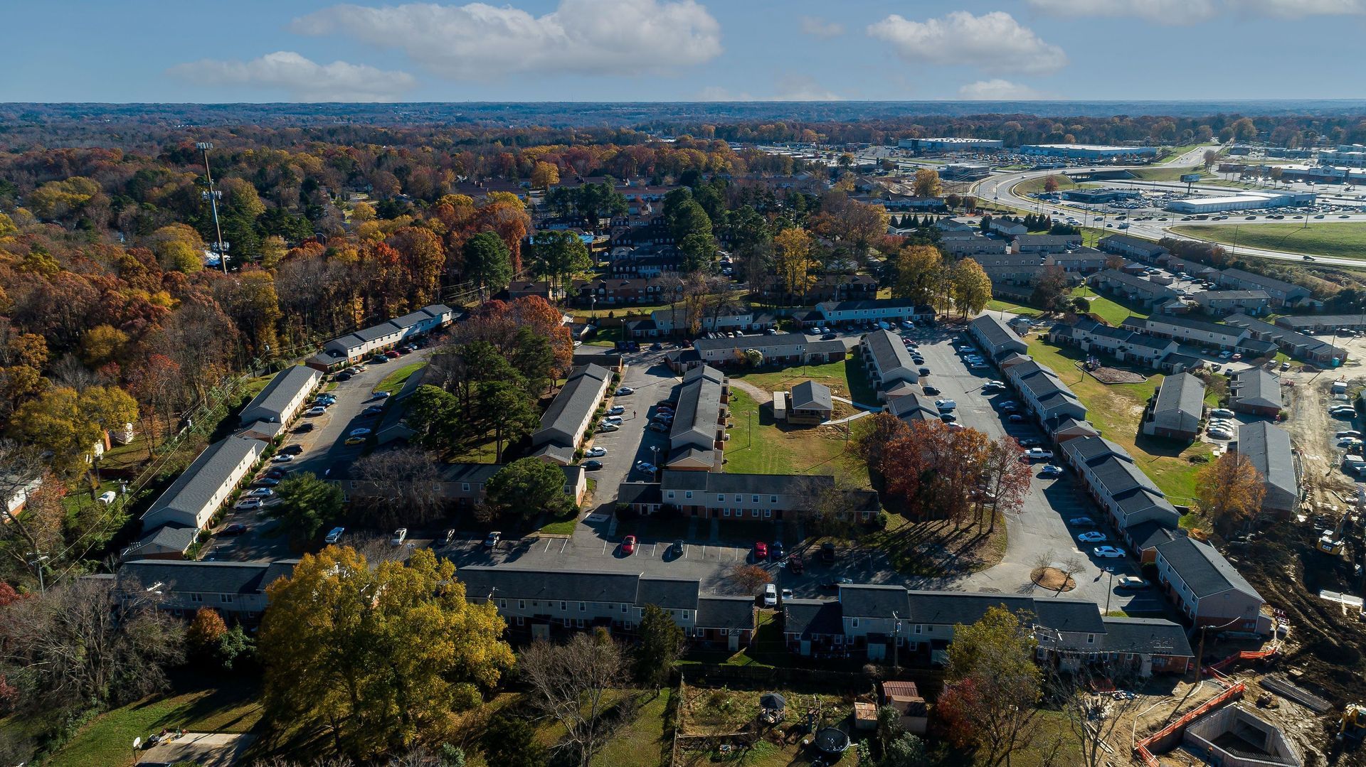 Aerial view of a large apartment complex surrounded by autumn trees and roads under a blue sky.