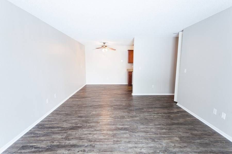 Empty apartment living area with wood-look flooring, neutral walls, and ceiling fan.
