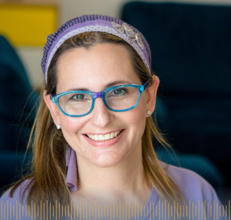 Woman with glasses and head covering smiles at camera.