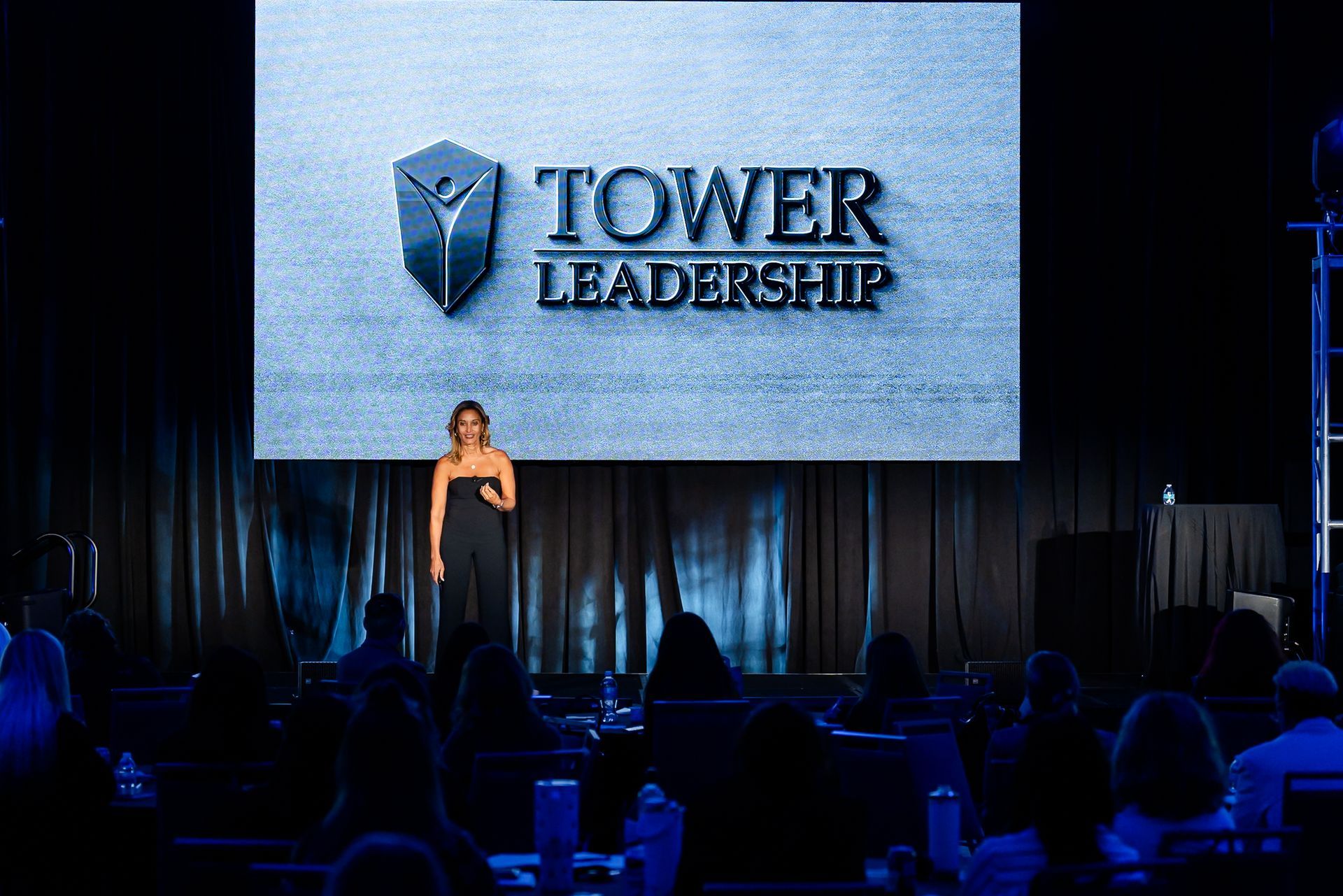 Woman presenting on stage beneath a large “TOWER LEADERSHIP” screen at a conference.