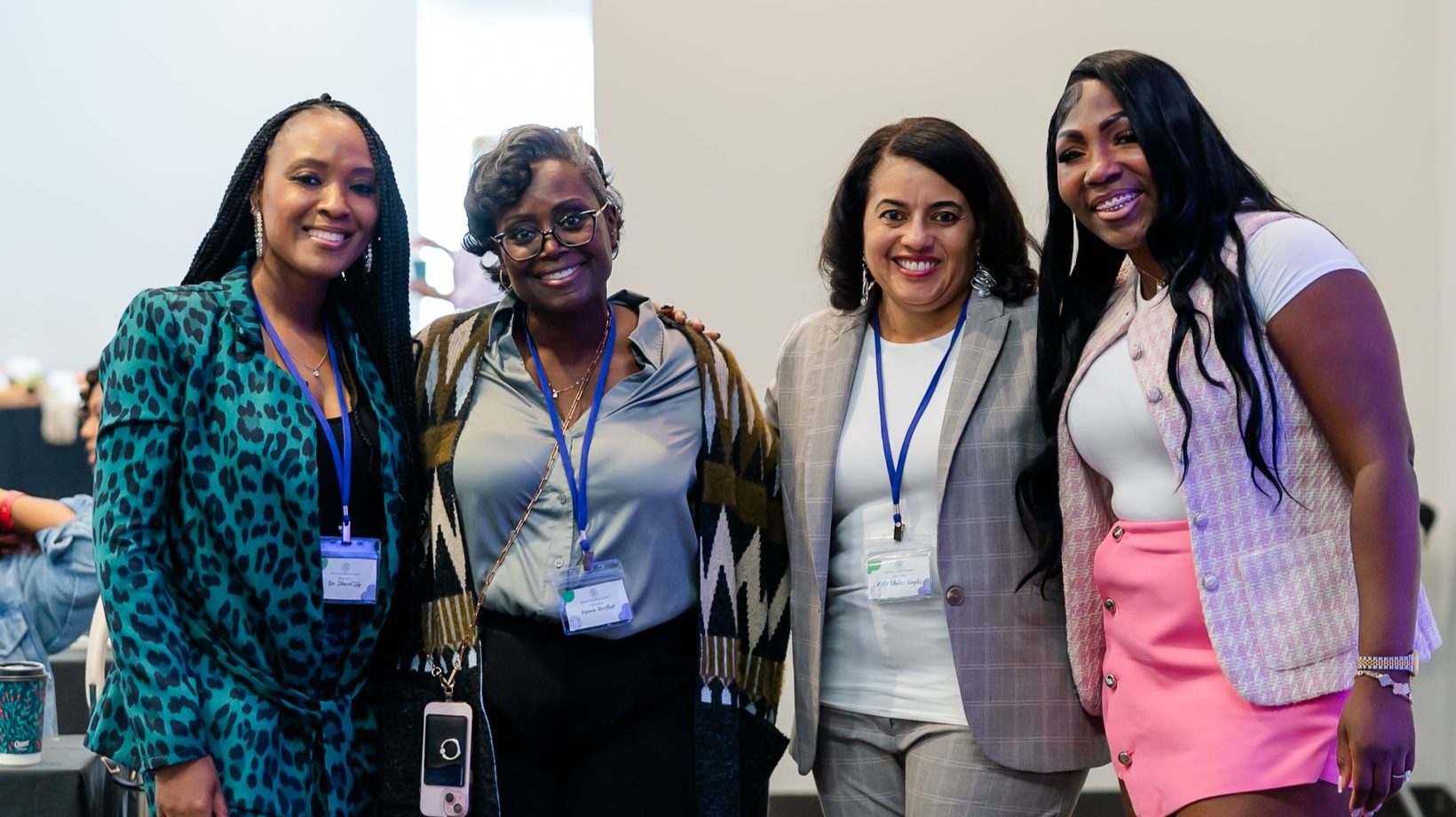 Group of people at an event, smiling and posing. Some have lanyards. Indoors, bright lighting.