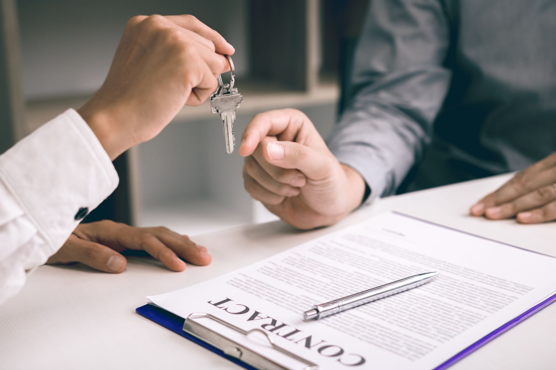 Person handing keys over a contract on a desk, a closing of a property deal.