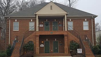 Two-story brick building with green doors and a front porch. Exterior stairs lead to both floors.
