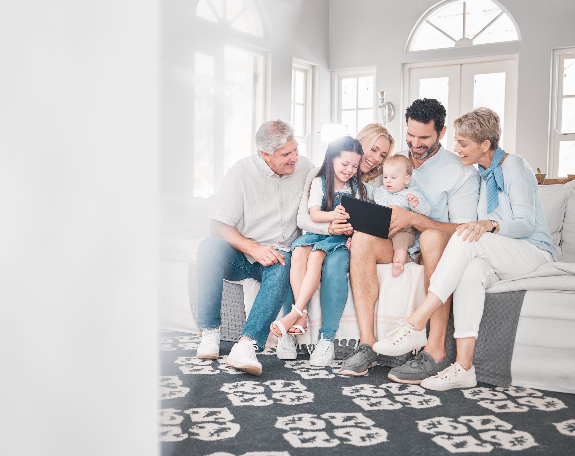 Family sitting on a couch looking at a tablet in a bright living room
