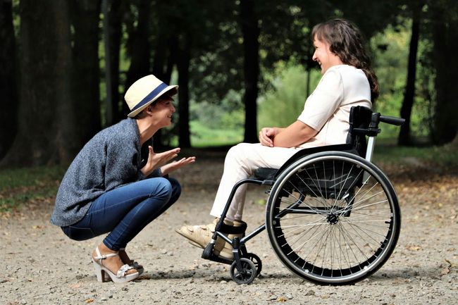 A woman is squatting down next to a woman in a wheelchair.
