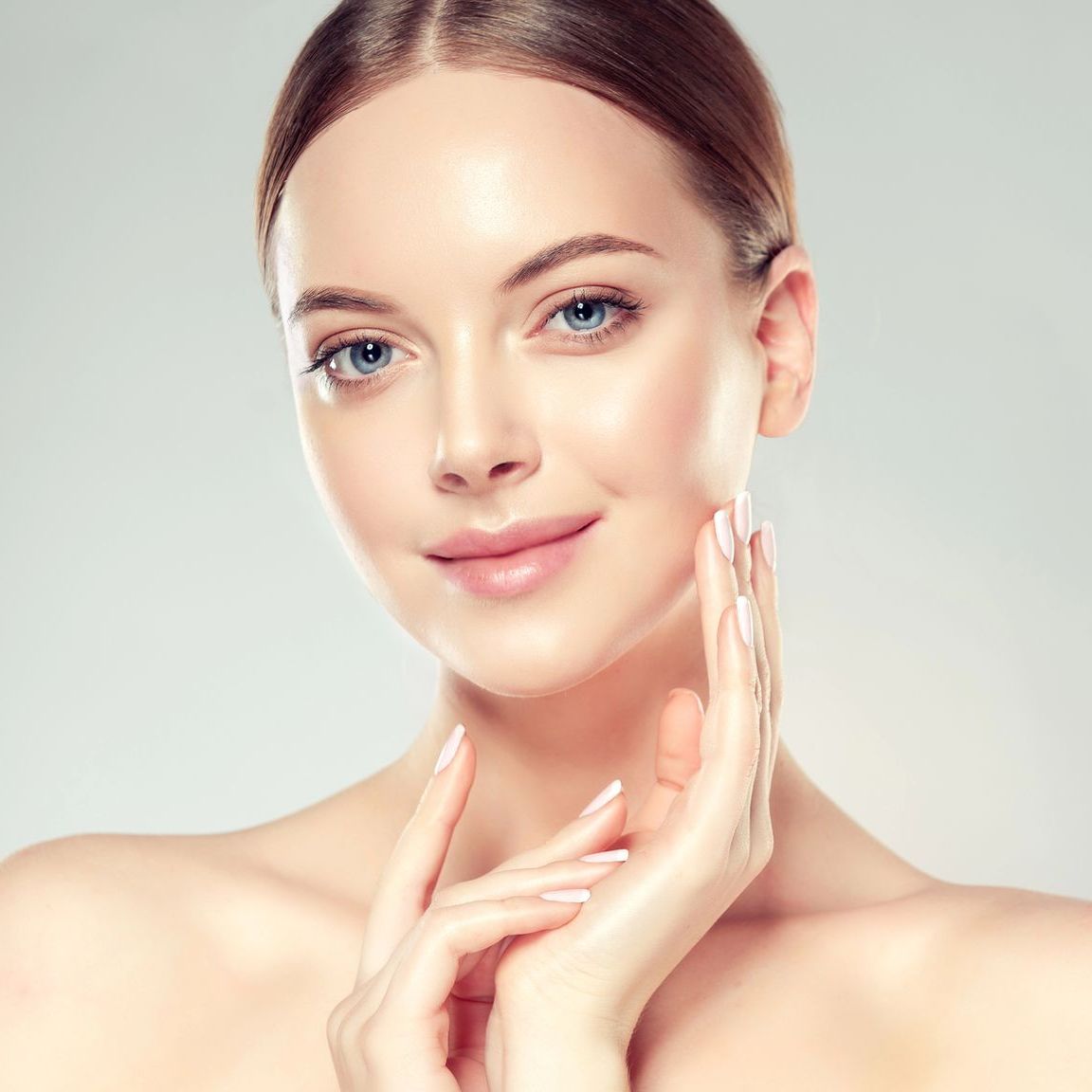 Woman with fair skin, blue eyes, and a slight smile, touching her face with both hands.