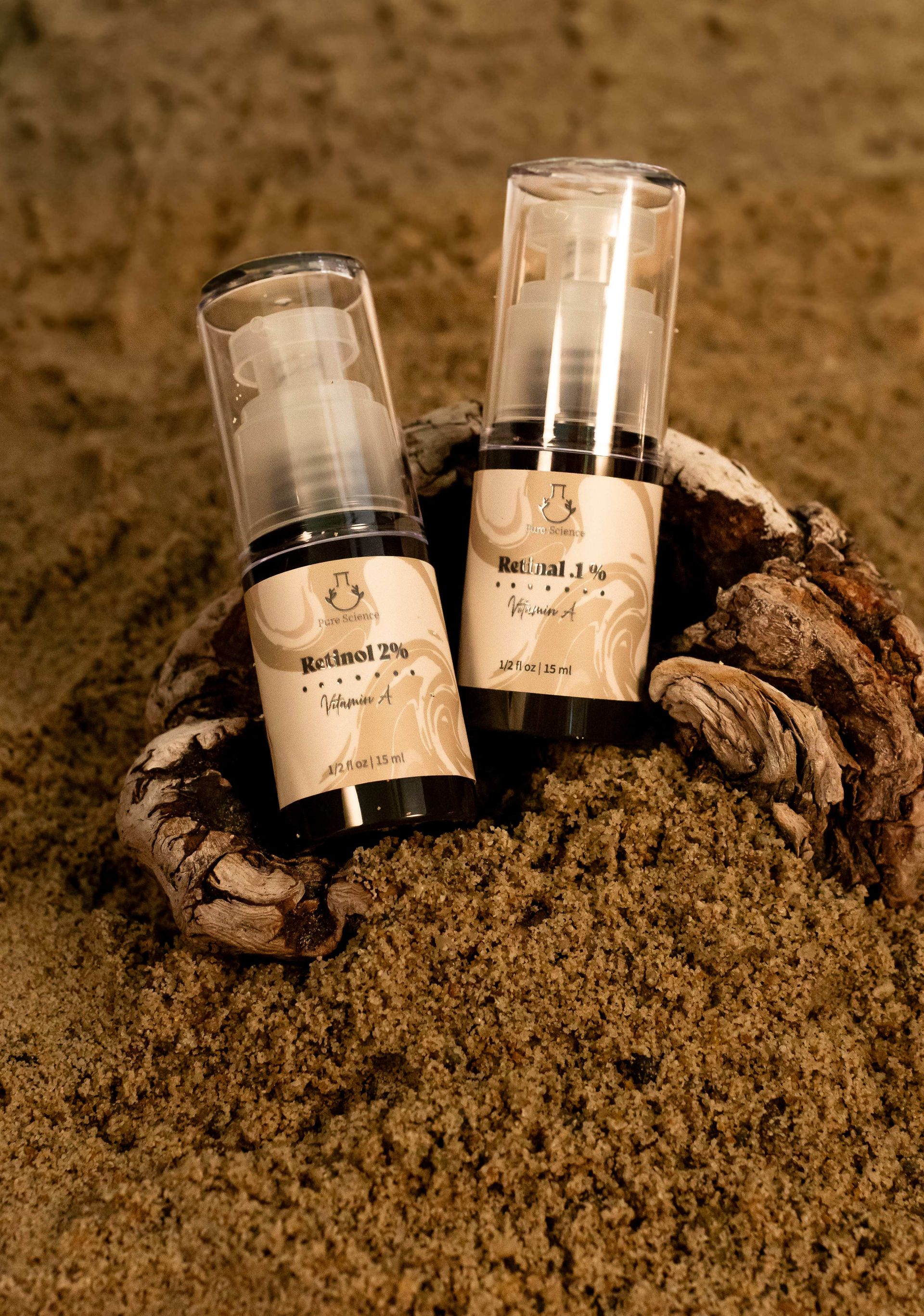 Two skincare product bottles with labels on sand.