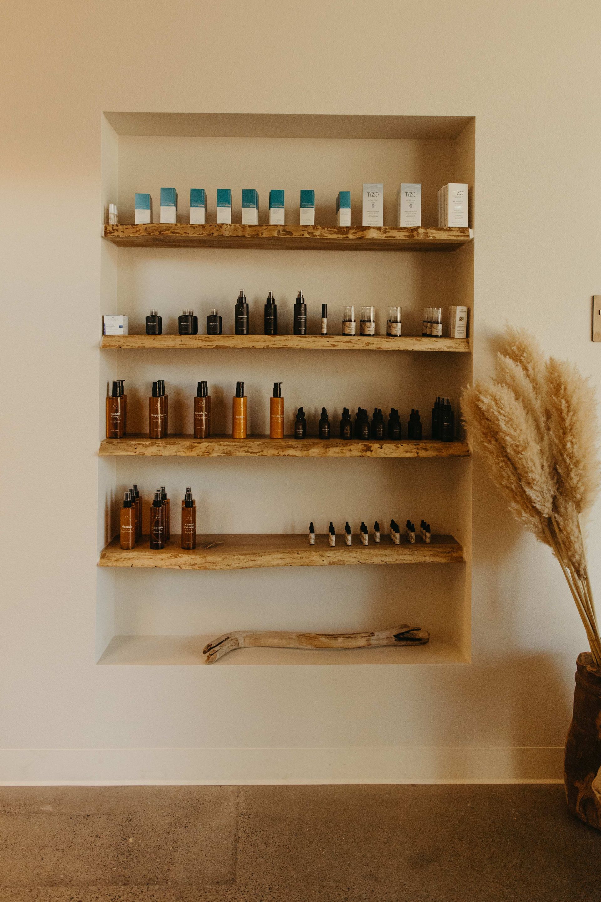 Built-in wooden shelves with skincare products in a cream-colored alcove. A vase with pampas grass sits nearby.