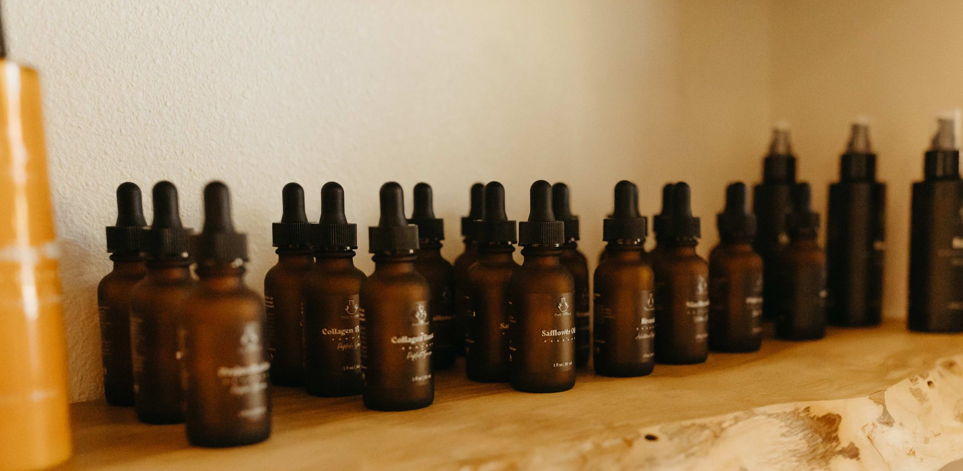 Row of small brown dropper bottles on a wooden shelf. White wall in the background.