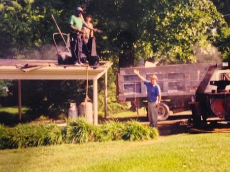 Two men standing on top of a roof next to a truck