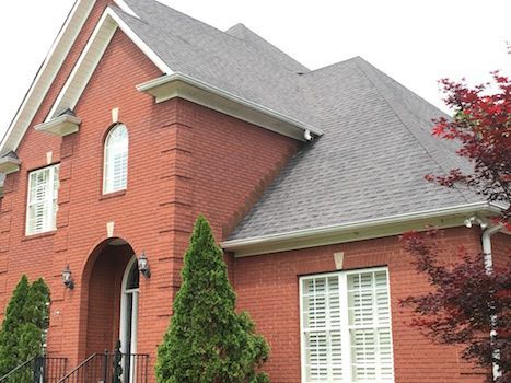 A large red brick house with a gray roof and white shutters.