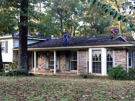 Two men are working on the roof of a brick house.
