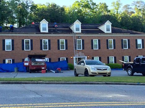 A white car is parked in front of a large brick building.