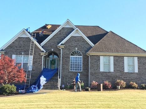 A man is working on the roof of a large brick house.