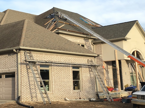 A crane is being used to install a roof on a brick house.