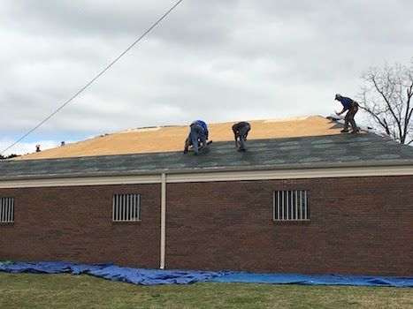 Two men are working on the roof of a brick building.