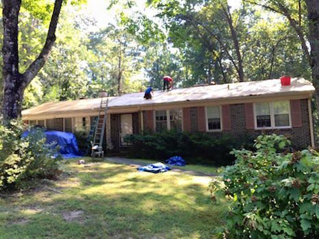 Two men are working on the roof of a brick house.