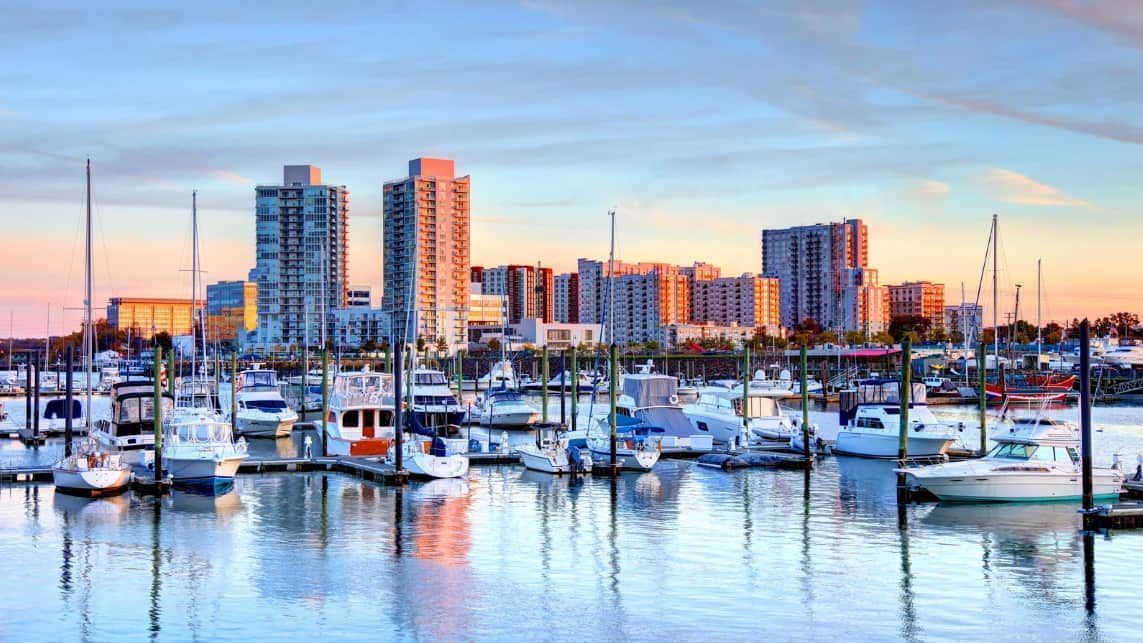 A marina with boats docked in front of a city skyline at sunset.