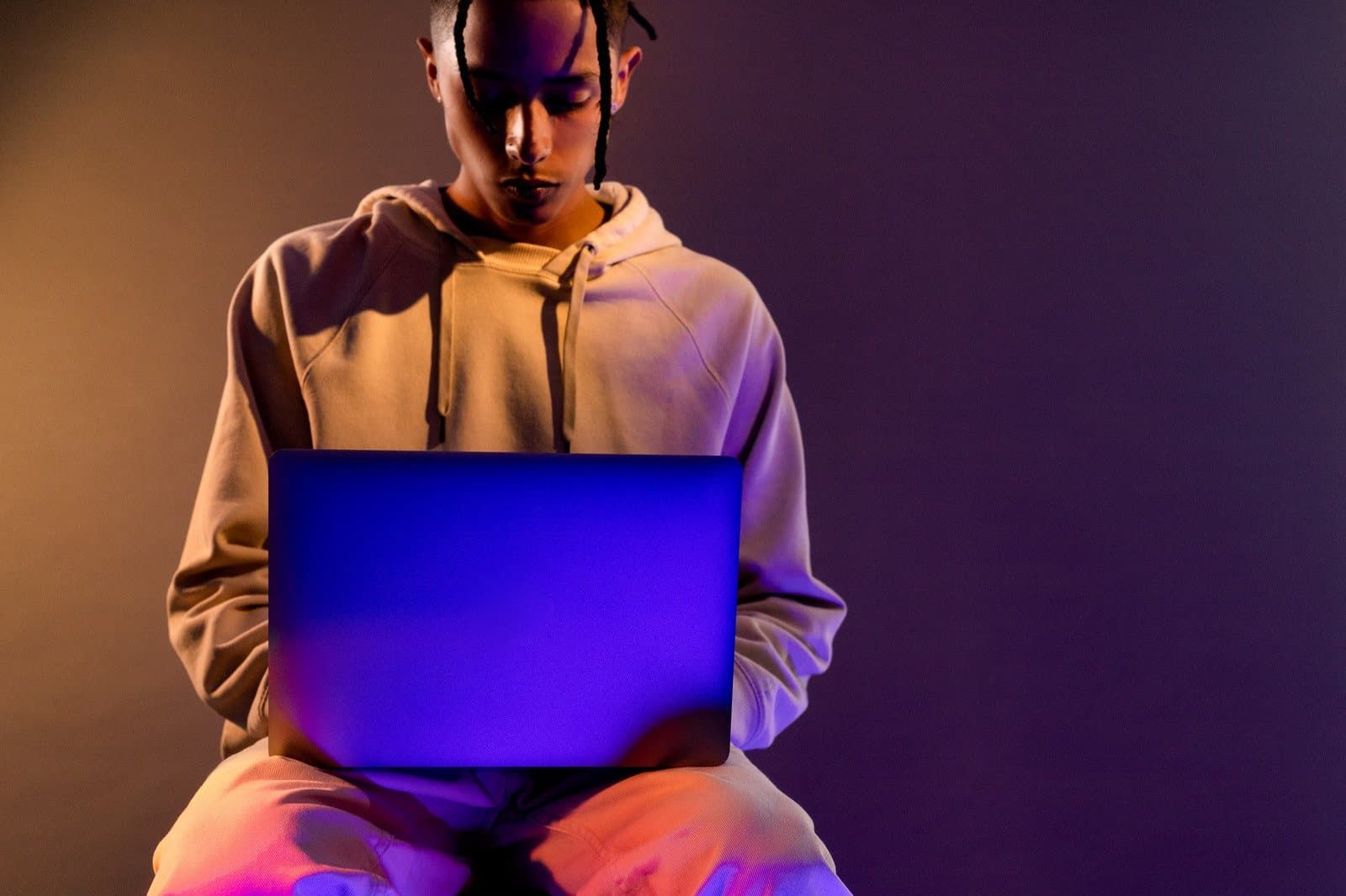 A man is sitting on a stool using a laptop computer.