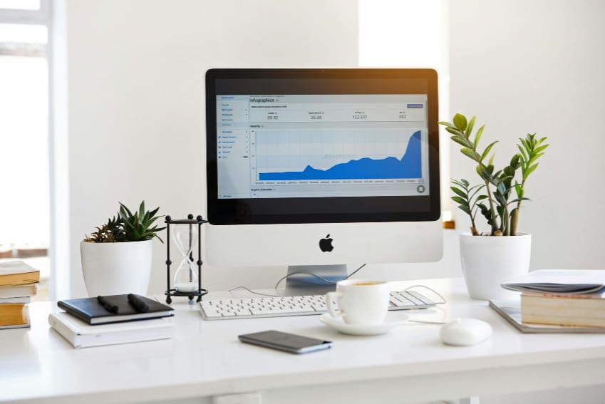 A computer is sitting on a desk next to a plant.