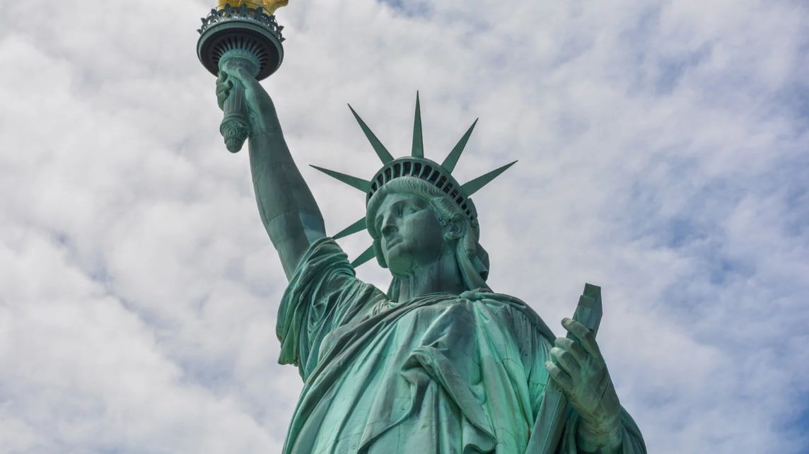 The statue of liberty is holding a torch in front of a cloudy sky.