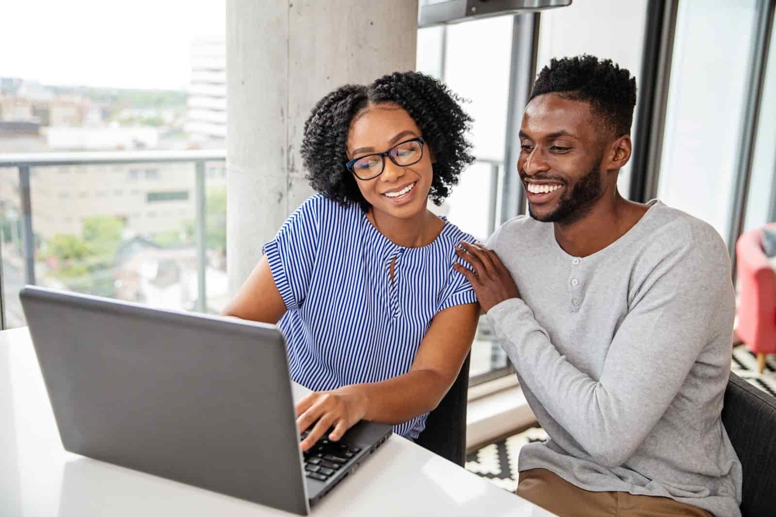 A man and a woman are sitting at a table looking at a laptop computer.