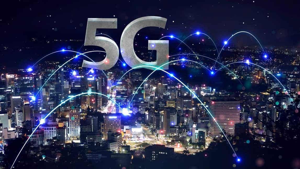 A city at night with a 5g sign in the foreground.