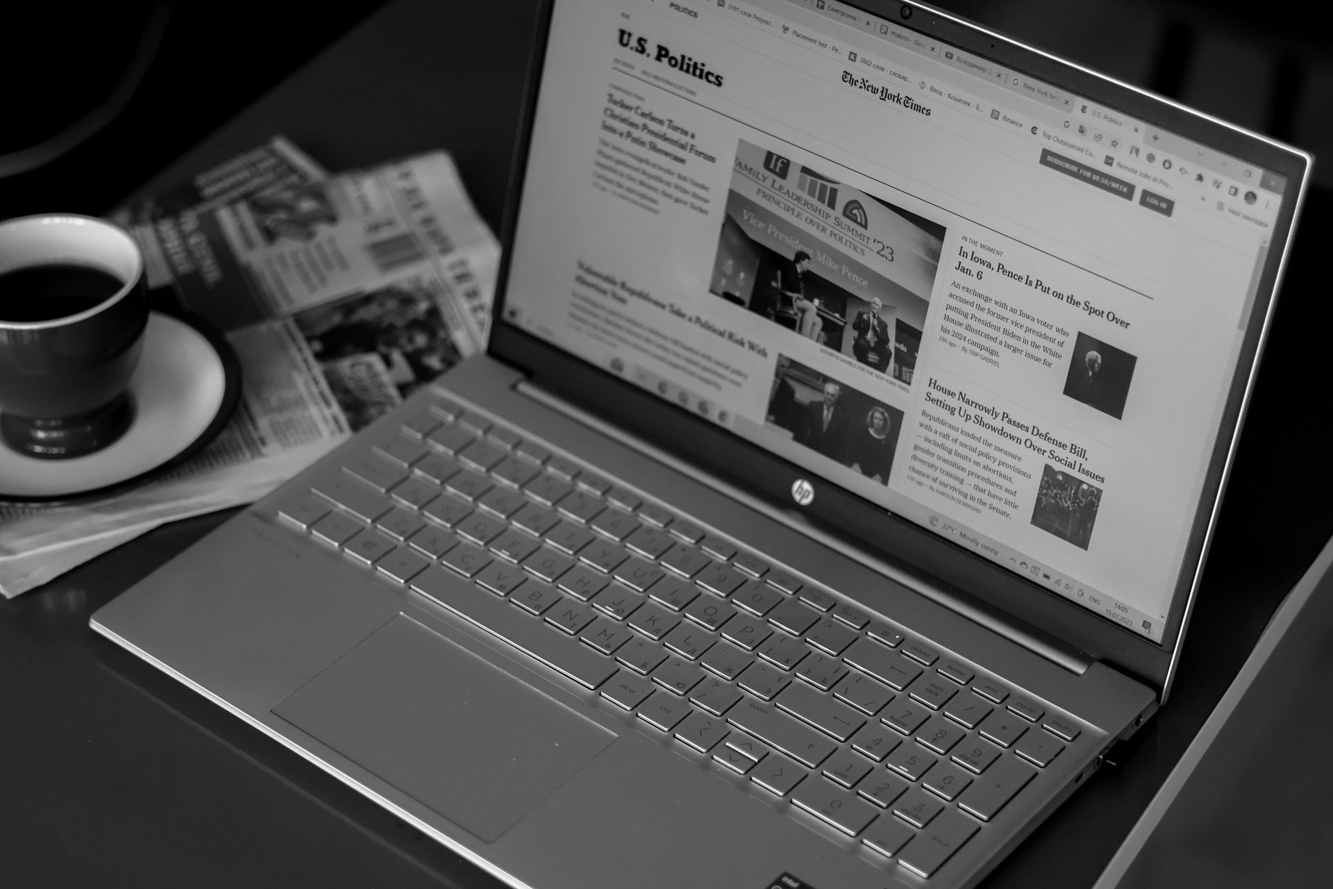 A laptop is open on a table next to a cup of coffee and a newspaper.
