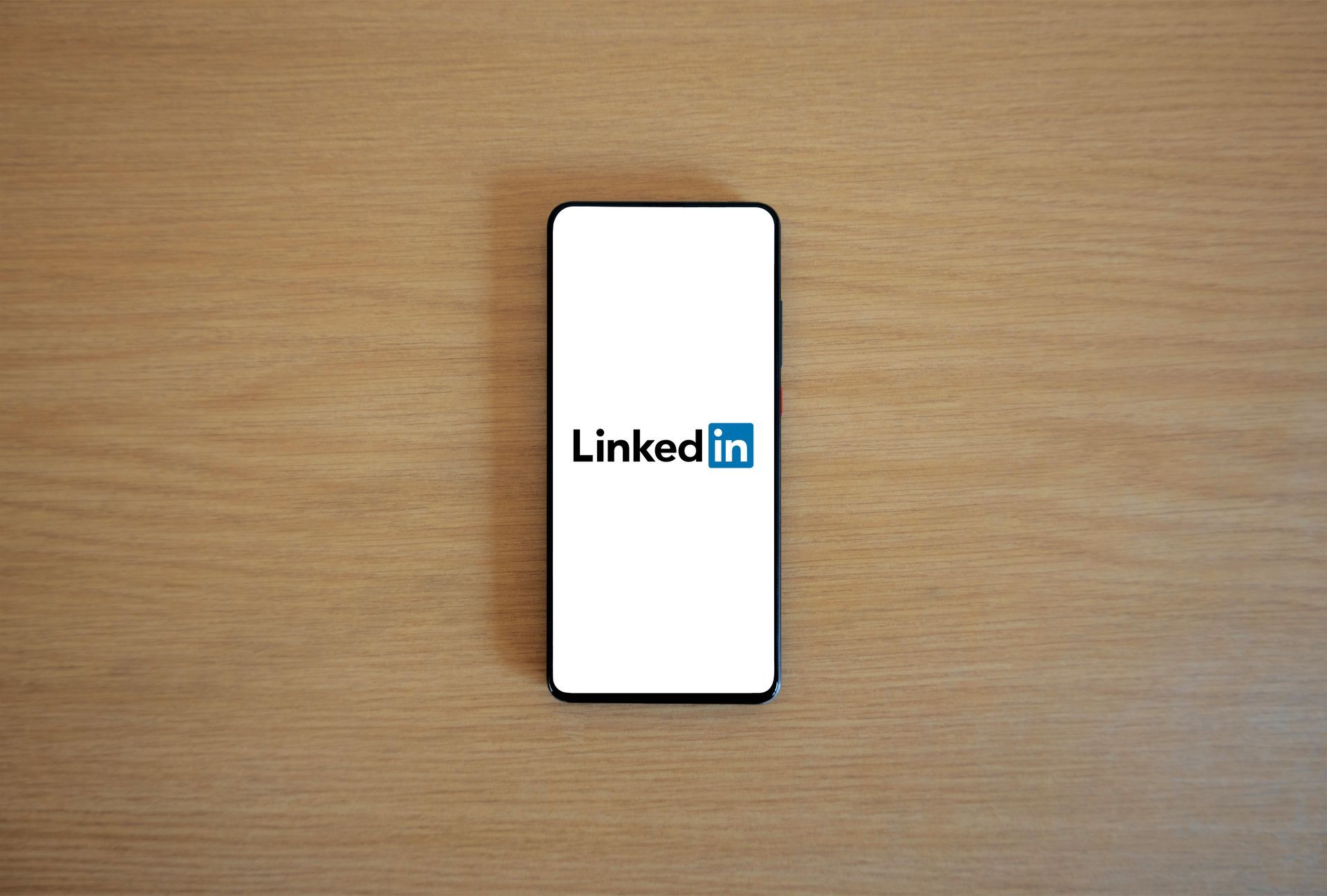 A cell phone with the linkedin logo on the screen is sitting on a wooden table.