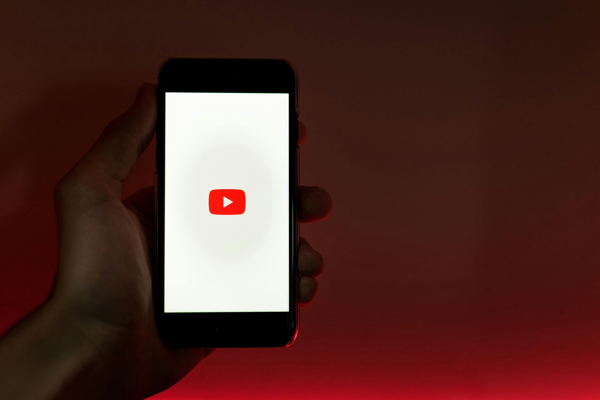 A person is holding a cell phone with a youtube logo on the screen.