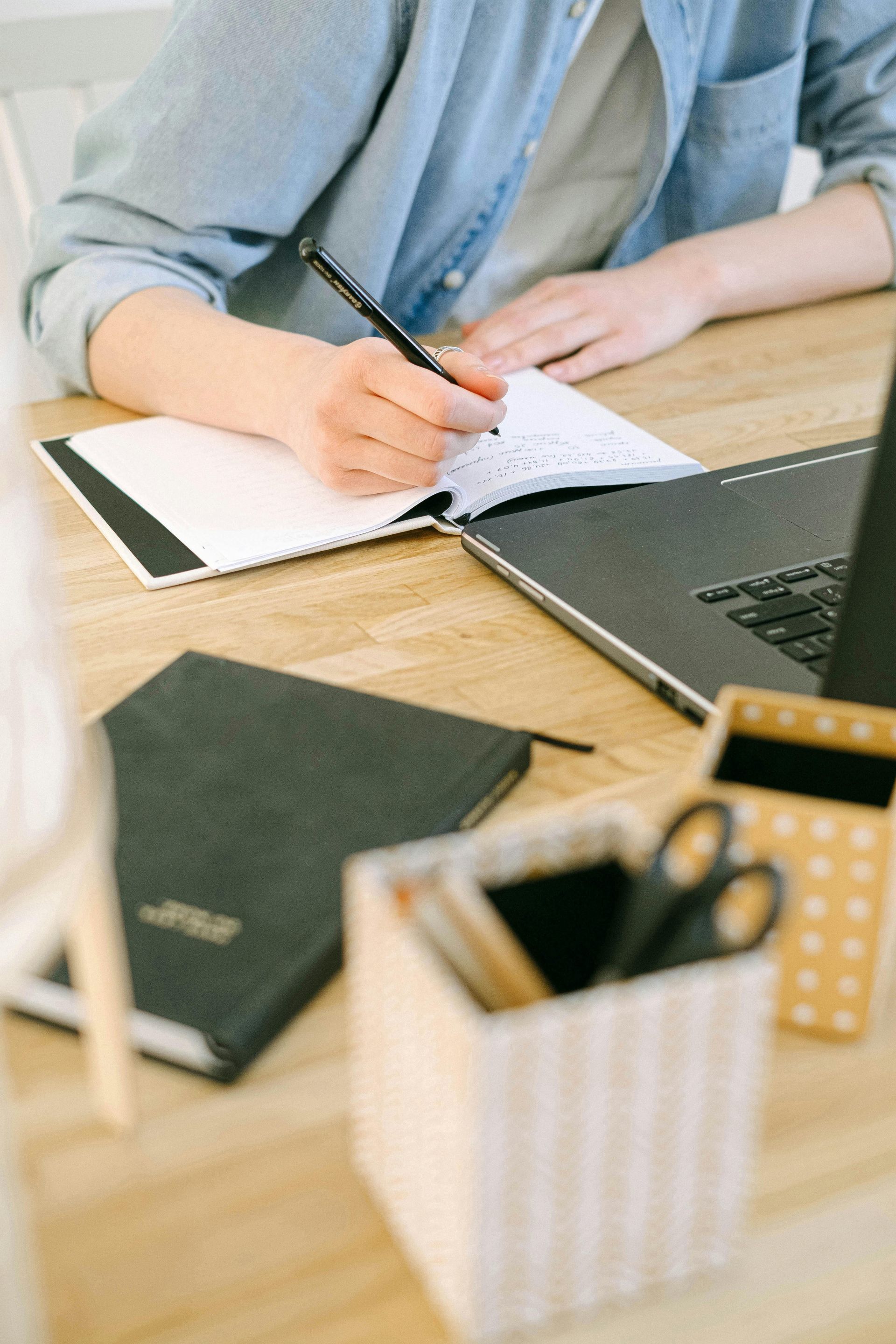 A person is sitting at a desk writing in a notebook.