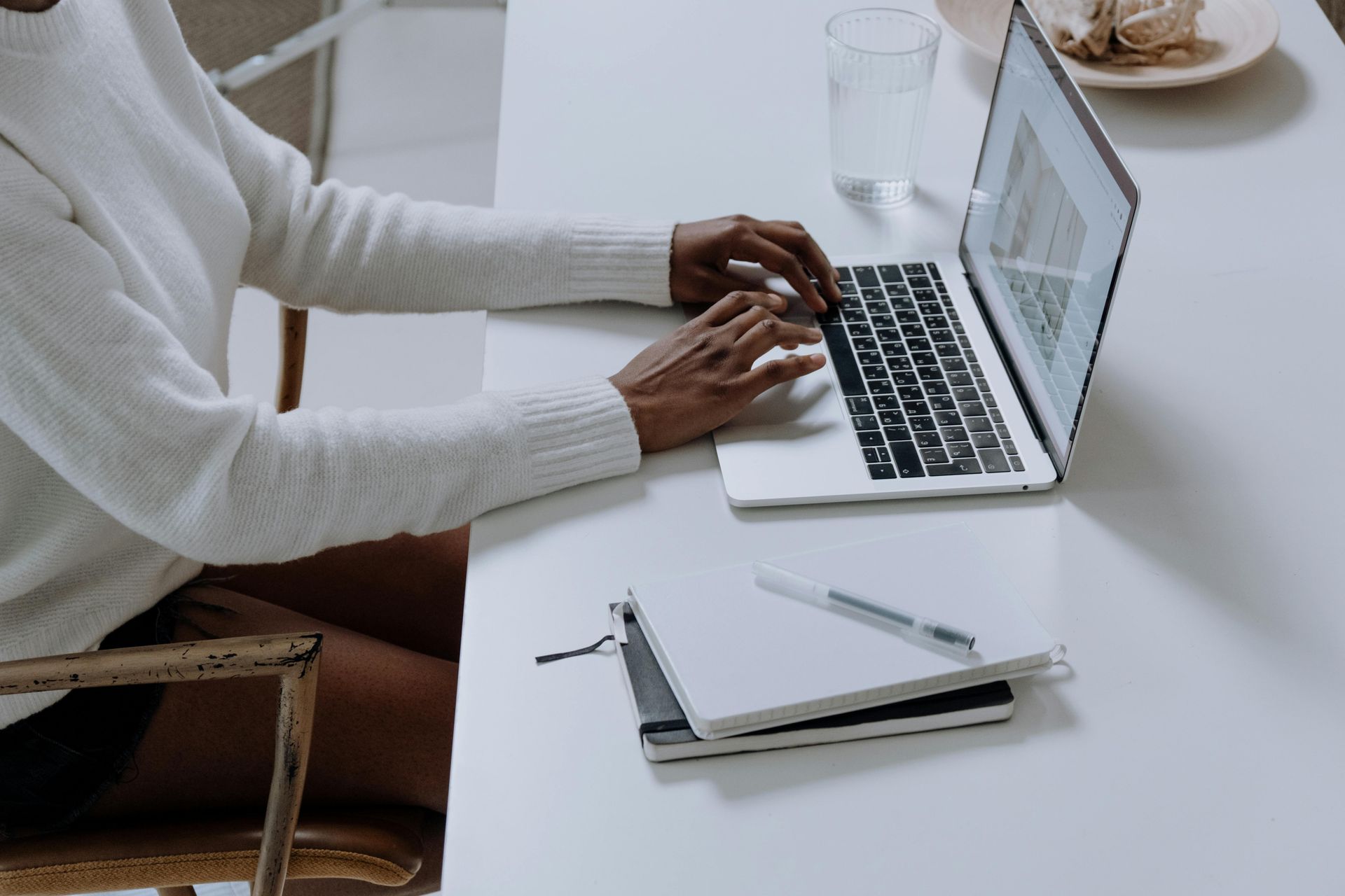 A woman is sitting at a desk typing on a laptop computer.